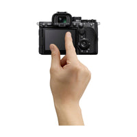 Hand touching the 4-axis touchscreen LCD on the back of a black Sony a7R VI mirrorless camera body.