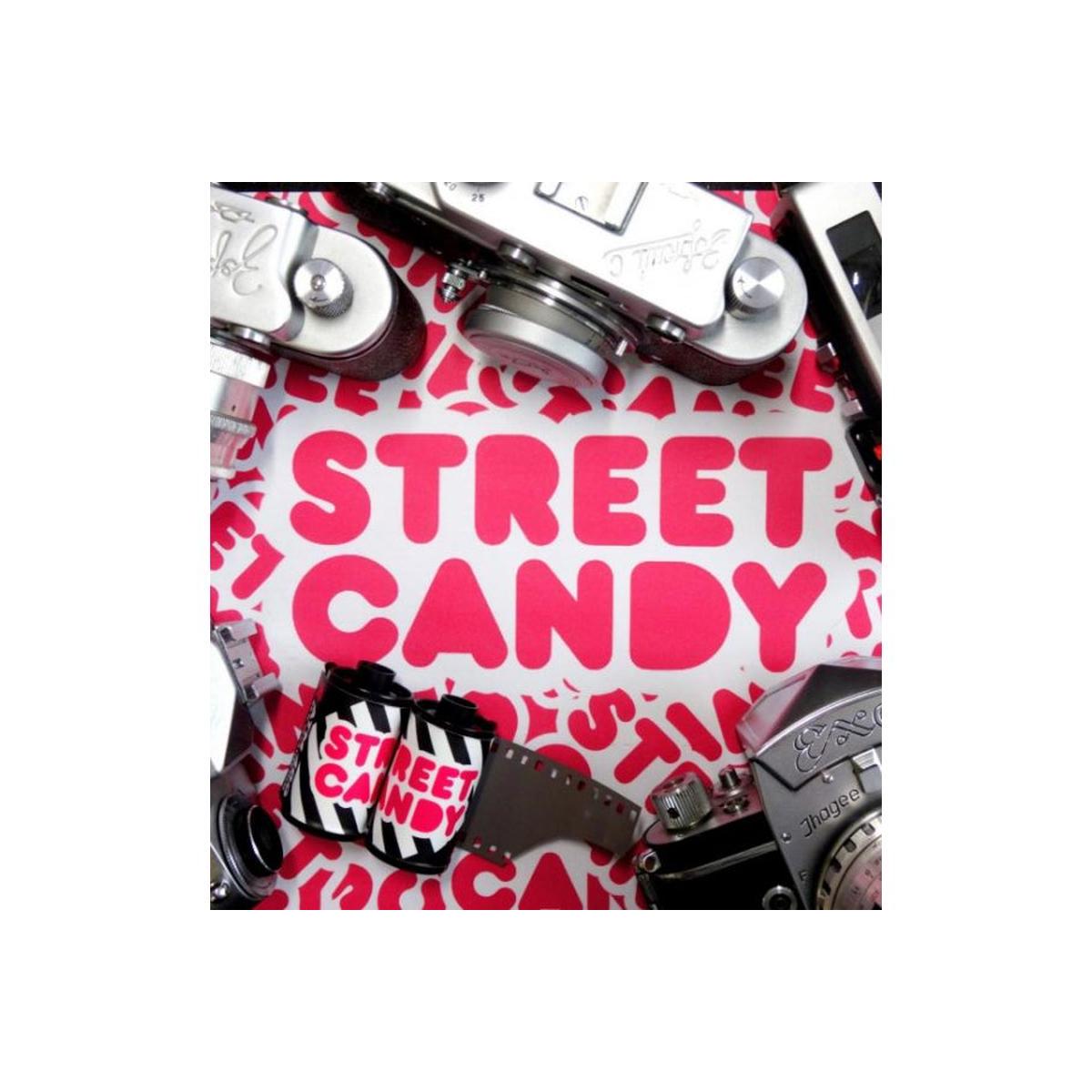 A styled flat-lay featuring vintage film cameras and a film strip around a white sheet printed with the words 'STREET CANDY' in bold pink letters.