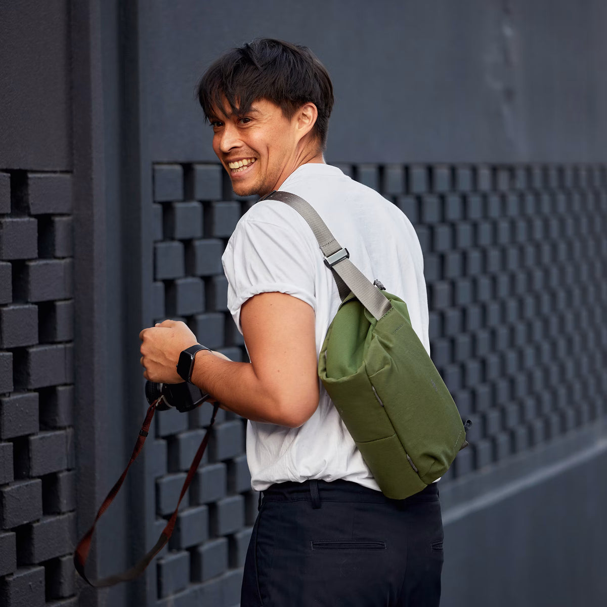 Man with a green bag leaning against a textured wall