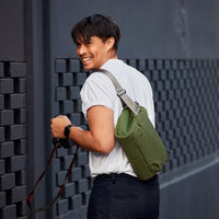 Man with a green bag leaning against a textured wall