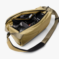 A tan camera bag with an open zipper, showing a camera and lens inside, on a light gray background.