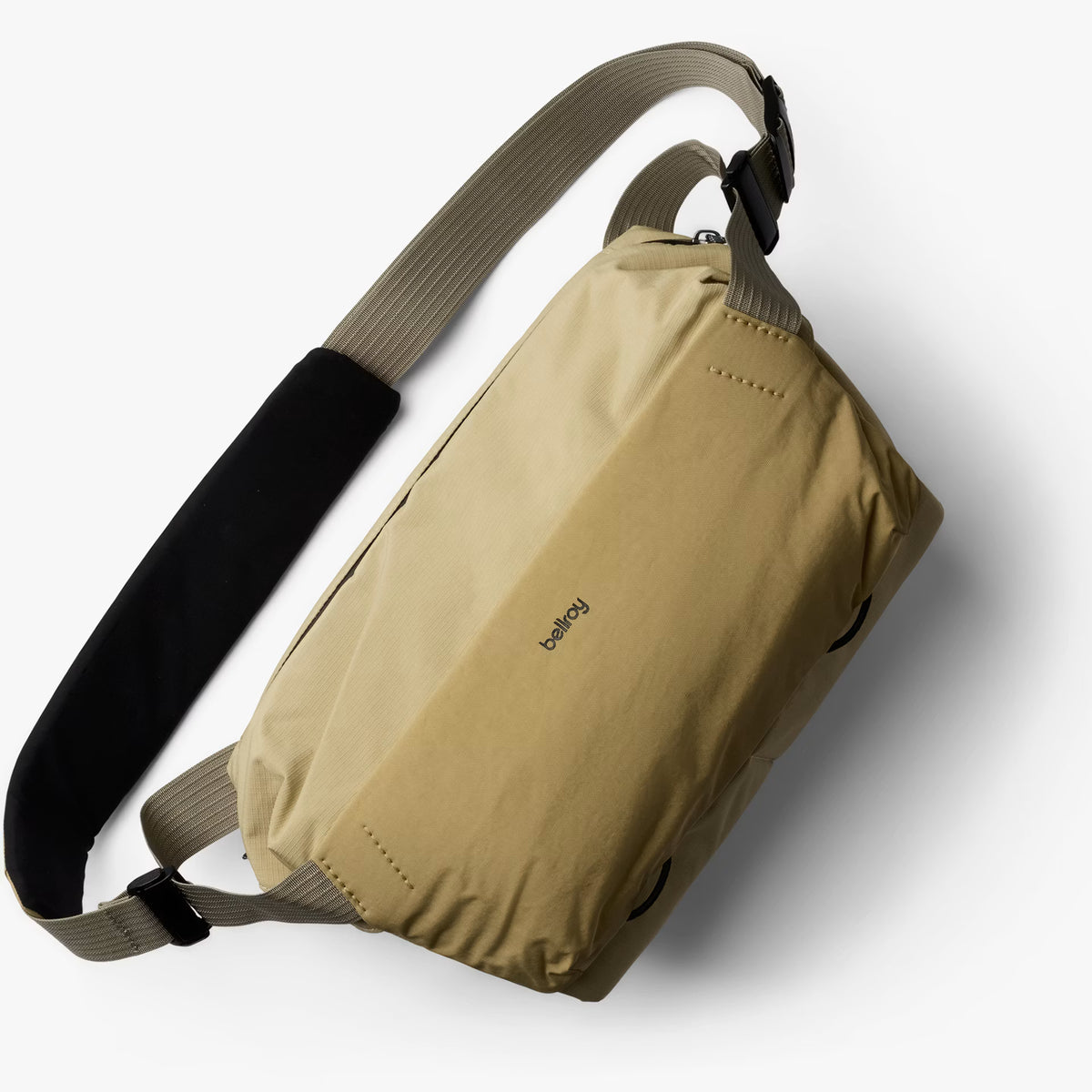 A beige waterproof dry bag sling backpack with a wide adjustable strap featuring a black padded section, shown on a light gray background.