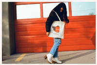 A woman holding a tote bag in in front of  red garage door