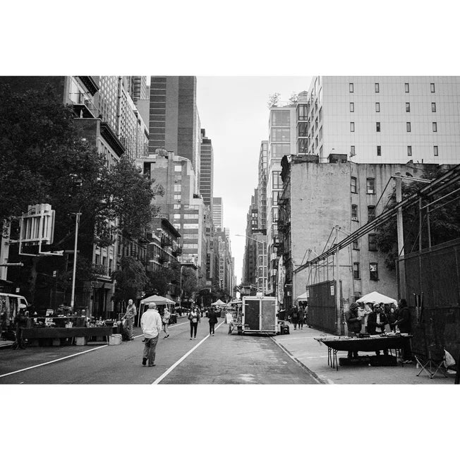 Black and white street photograph of a city scene with tall buildings, pedestrians, market stalls, and a bus in the middle of the road.