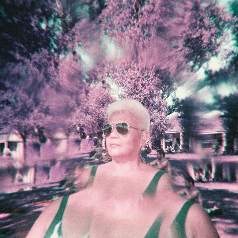 Person with platinum blonde hair wearing sunglasses and a swimsuit in a pool setting.