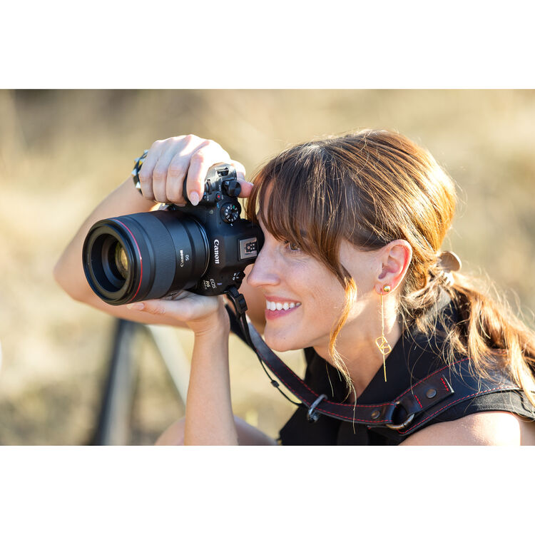 Woman holding a Canon camera outdoors with a blurred natural background
