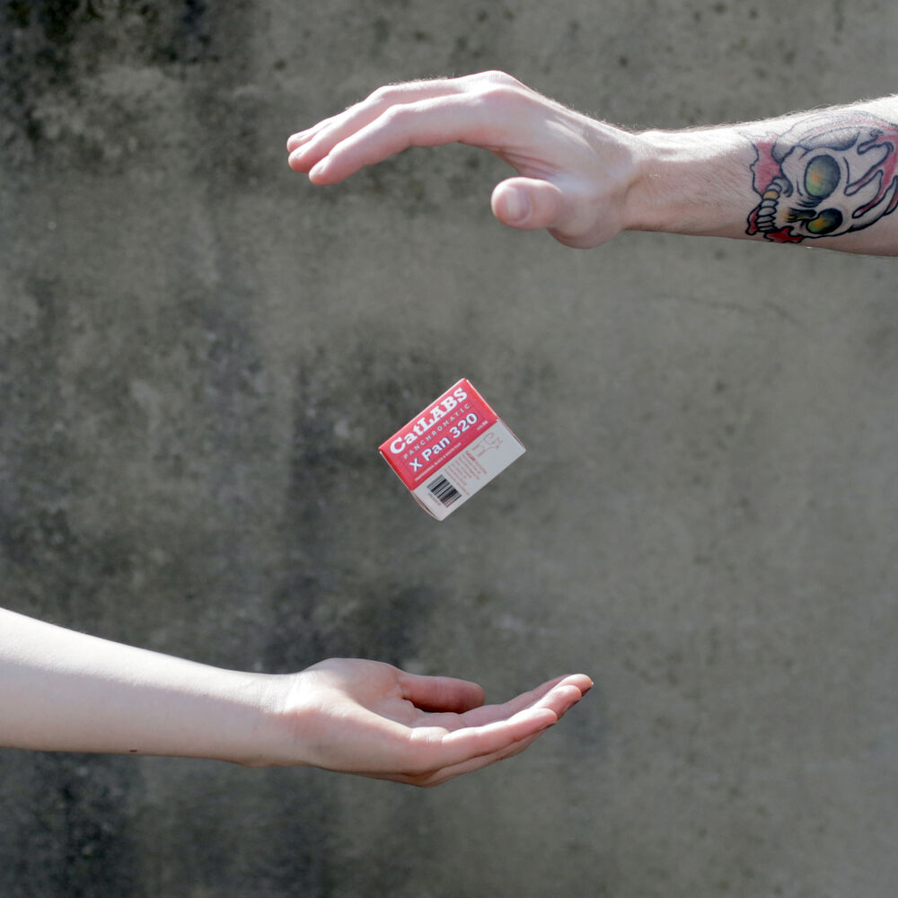 A small red and white 'Carnivore' food label floating between two human hands against a textured gray concrete wall.