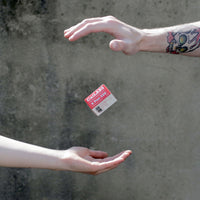 A small red and white 'Carnivore' food label floating between two human hands against a textured gray concrete wall.