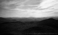 Black and white landscape of rolling hills with a cloudy sky.