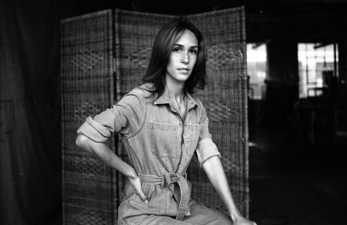 Black and white photo of a person wearing a jumpsuit with a woven screen in the background