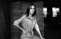 Black and white photo of a person wearing a jumpsuit with a woven screen in the background