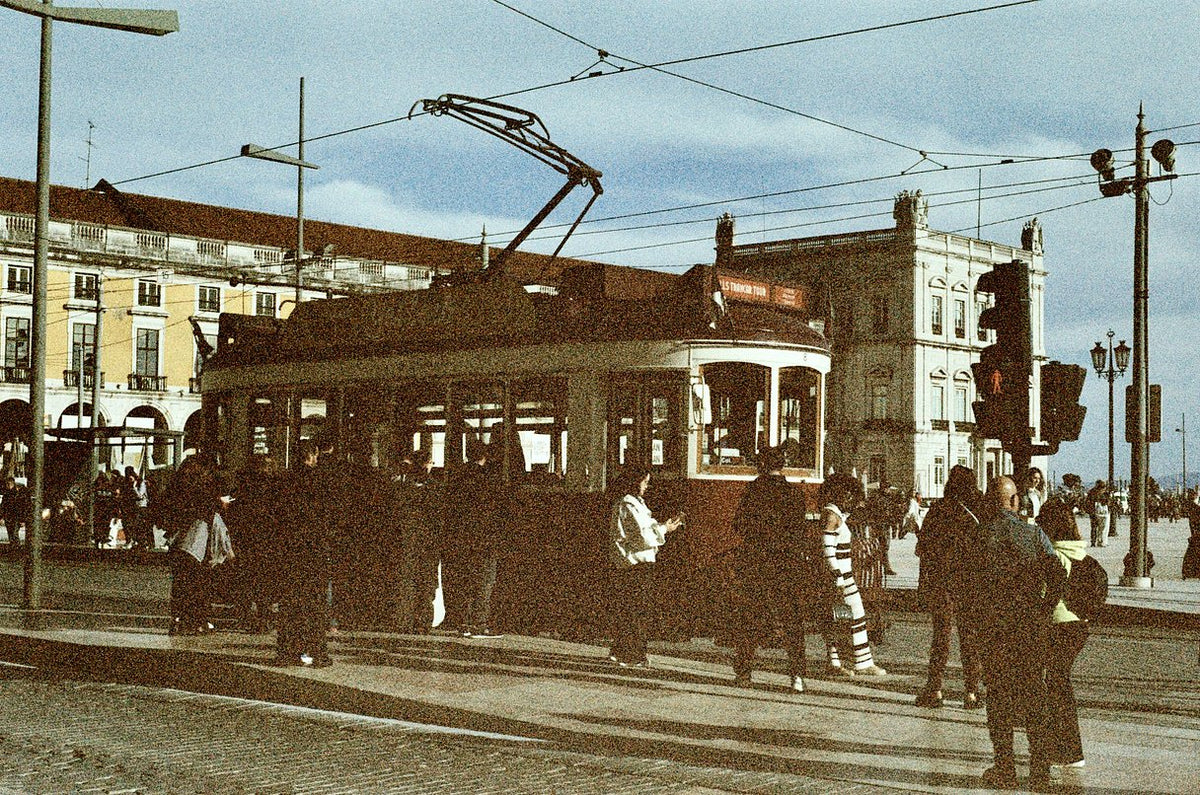 Vintage street scene with a tram at a crossroad, surrounded by pedestrians, buildings, overhead wires, and traffic lights, rendered in a warm sepia tone.