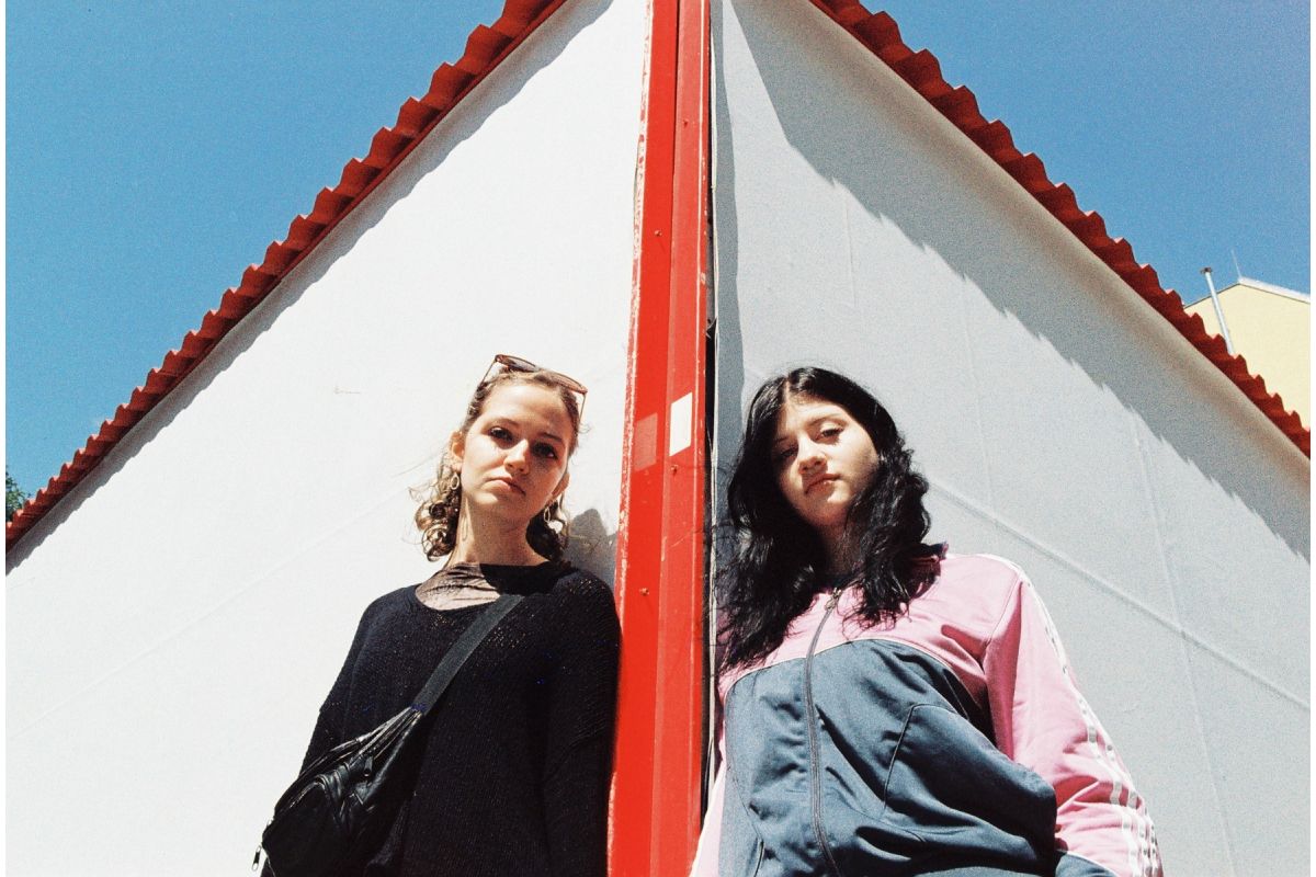 Two women standing next to a red and white building with a clear blue sky.