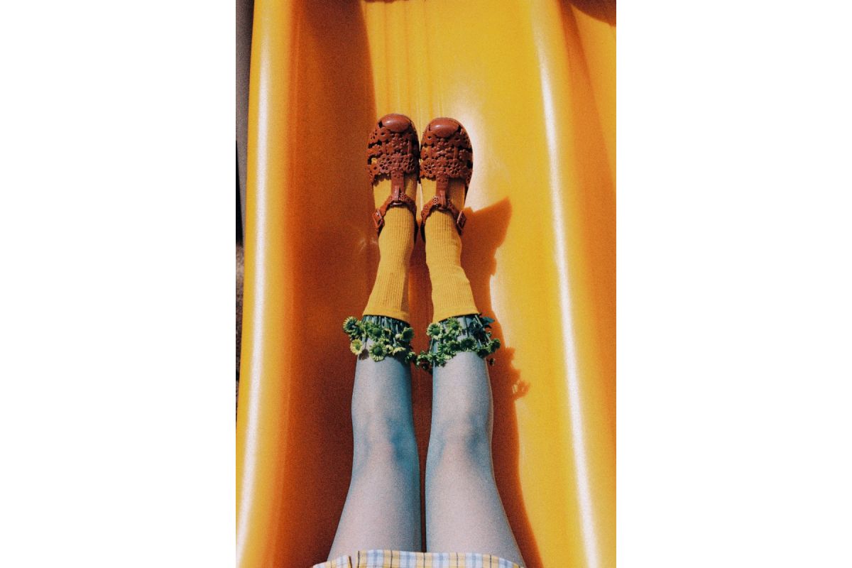 Person sliding down a yellow slide wearing patterned shoes and tights.