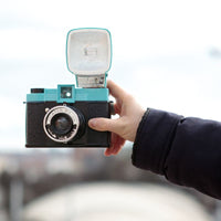 Hand holding a vintage camera with a blurred cityscape in the background