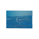 A square photographic print or canvas featuring a blue-toned cityscape at dusk, with rooftops, distant lights, and a hazy skyline, centered on a plain white background.