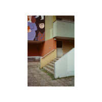 A square art print depicting an architectural courtyard with stairs, a mural, and a modern building facade, centered on a white background.