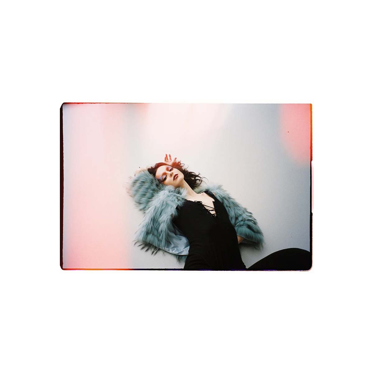 A square photographic print or poster featuring a woman reclining against a pale background with pink and orange light leaks, shown centered on a plain white background.