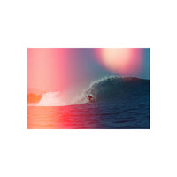 A square art print or poster showing a surfer riding inside a large ocean wave, with a pink-to-blue color gradient and a soft glowing circular light in the sky, centered on a white background.