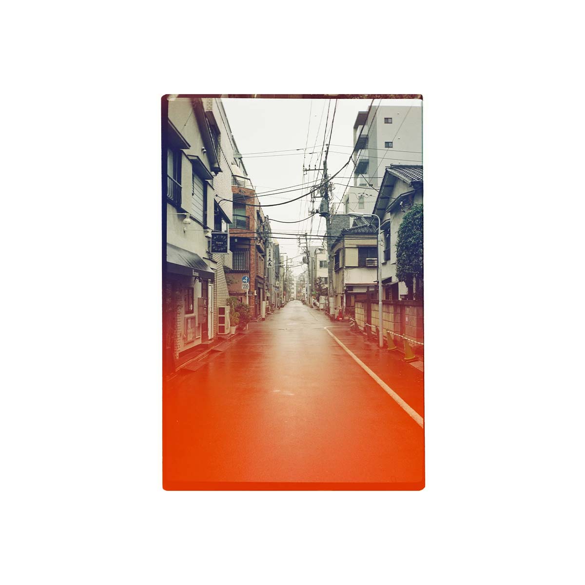 A vertical photographic print of a narrow urban street lined with buildings, shown centered on a plain white background. The print has a warm orange-red border and a muted, slightly vintage-toned street scene inside.