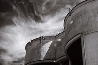 Black and white architectural photograph of curved concrete structures against a dramatic cloudy sky.