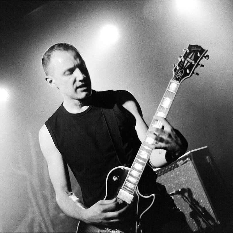 Black and white photo of a man playing an electric guitar on stage under dramatic spotlighting.