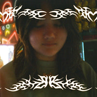 A person with long dark hair wearing a dark green t-shirt, standing in a brightly lit arcade or game center with colorful neon lights in the background. The image has a heavy white tribal graphic overlay on the top and bottom borders.