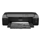 A Canon PIXMA PRO-310 all-in-one ink printer in black, shown from a front-facing angle with a black-and-white landscape photograph emerging from its paper tray against a solid white background.