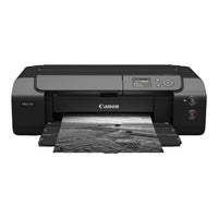 A Canon PIXMA PRO-310 all-in-one ink printer in black, shown from a front-facing angle with a black-and-white landscape photograph emerging from its paper tray against a solid white background.