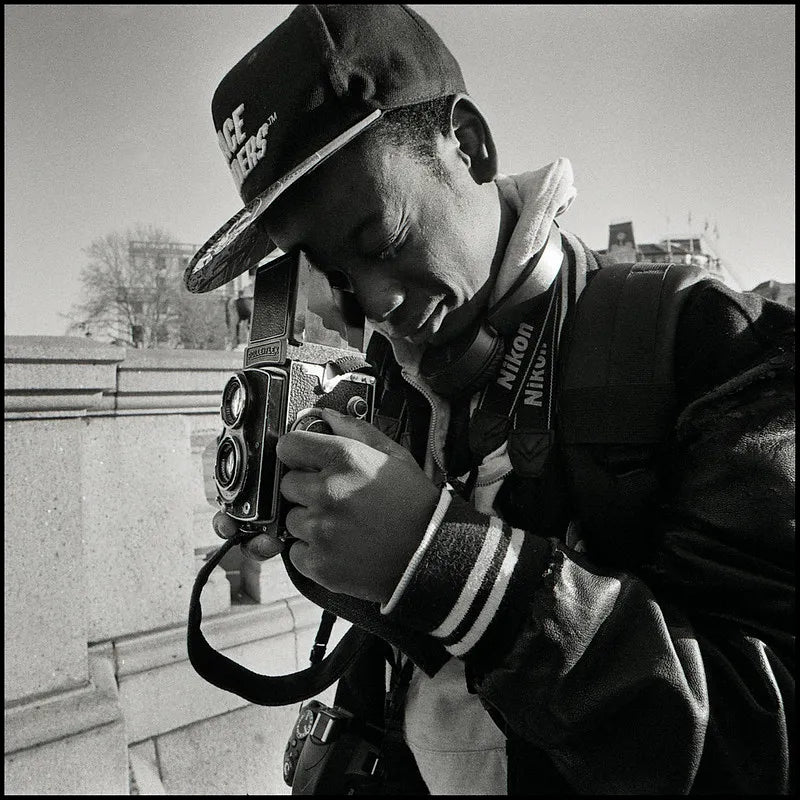 Black and white image of a man with a ball cap look thru a vintage camera with twin lenses