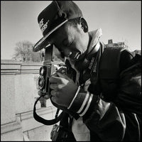 Black and white image of a man with a ball cap look thru a vintage camera with twin lenses