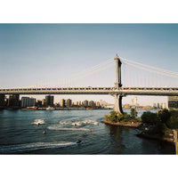 Manhattan Bridge over the East River with boats and city skyline in the background