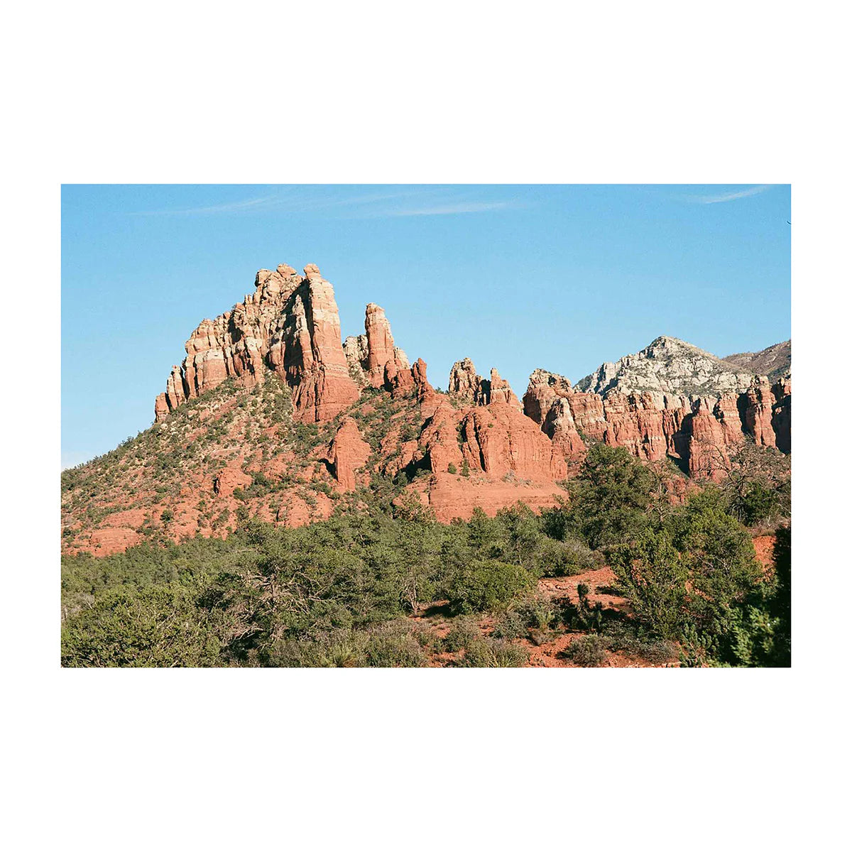 Red rock mountains and greenery with a blue sky photograph on a white background