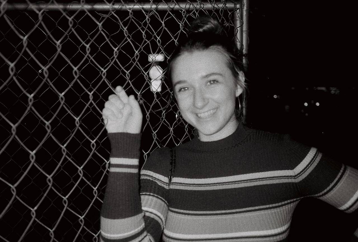 black and white photograph of a girl smiling by a fence