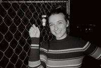 black and white photograph of a girl smiling by a fence