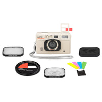 A vintage-style beige camera kit on a white background, including a beige camera body with red text, a wrist strap, a close-up lens, a kioskcope lens, a splitter lens, colorful filter pieces, and a black case.