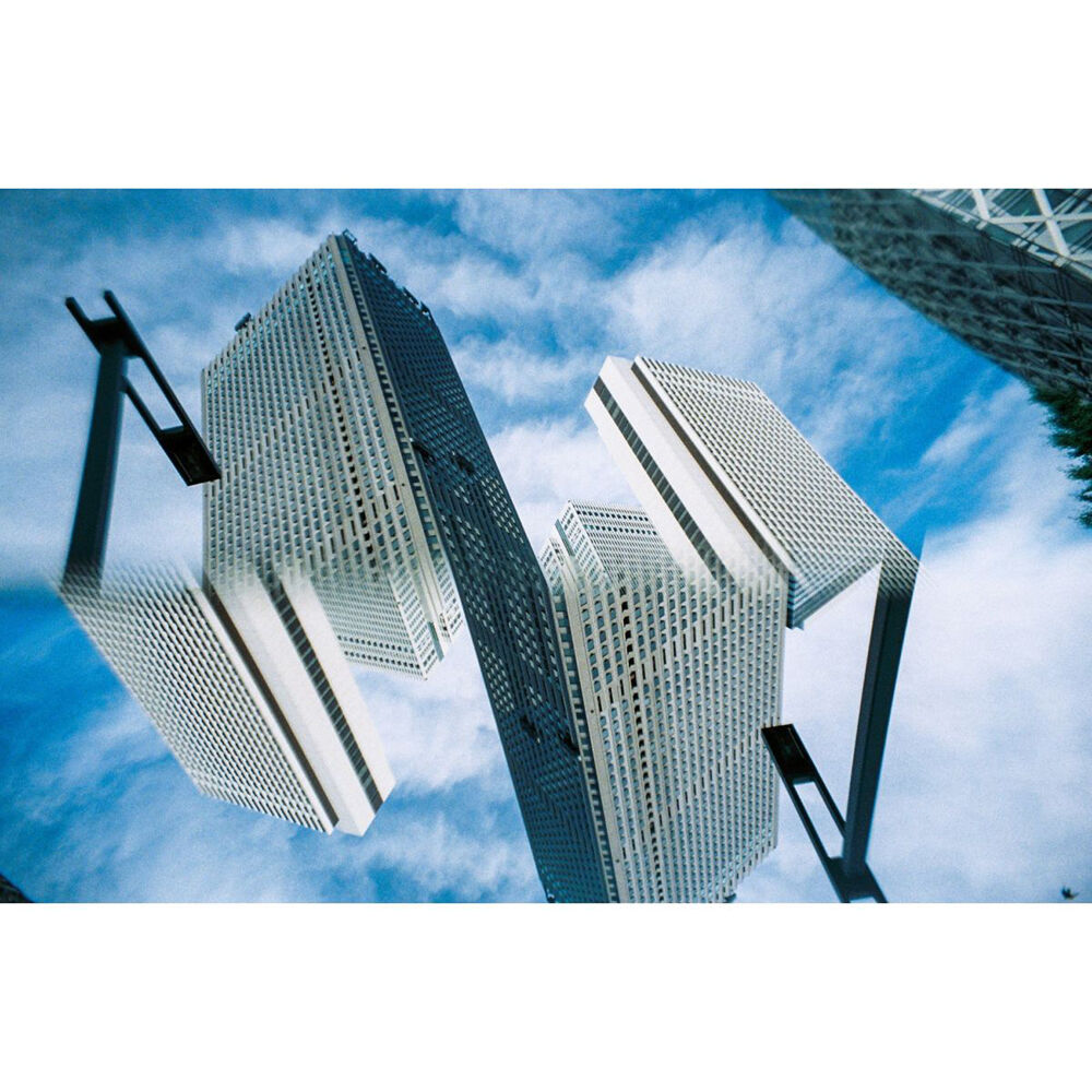 An architectural photograph of modern skyscrapers with a white grid pattern, captured from a dramatic low angle against a blue sky with white clouds.