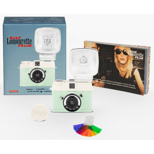 Half Lomovrette Frame instant camera kit with a mint green and cream camera body, a large white flash, its blue retail box, a smaller printed insert card, a round white lens cover, and a small multicolor color card on a white background.
