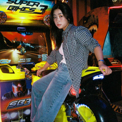 Person sitting on a yellow toy motorcycle in front of a 'Super Bikes' arcade game.
