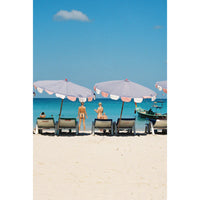Beach scene with people under large umbrellas and a clear blue sky.