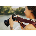 Person holding a camera with a strap, outdoors near water