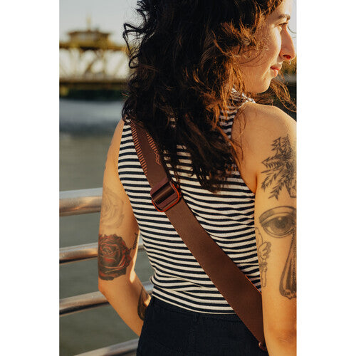 Person wearing a striped tank top with tattoos on arms by a waterfront
