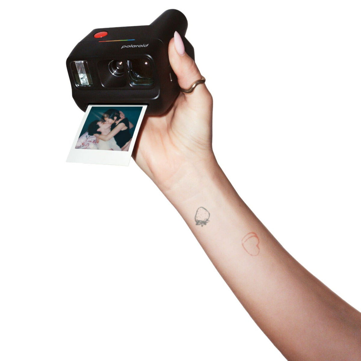 A hand holding a black Polaroid instant camera that is pulling a printed photo strip out, shown against a plain white background.