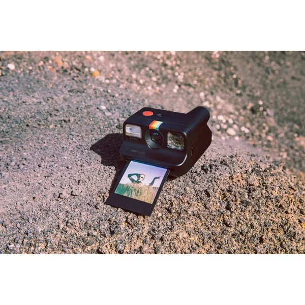 black polaroid go camera with go film with black borders placed on a large rock surface