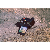 black polaroid go camera with go film with black borders placed on a large rock surface