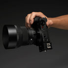 A hand holding a black film camera with a large lens attached, shown against a dark gray studio background.