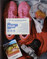 A styled flat-lay of a travel packing box containing pink sneakers, a Polaroid camera, a vintage camera, a pair of glasses, a bag of ColorPlus contact lenses, and a printed card reading 'For the world travelers: FILM'.