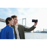 Two people taking a selfie with a bridge and city skyline in the background