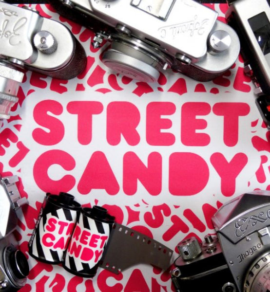 A styled flat-lay featuring vintage film cameras and a film strip around a white sheet printed with the words 'STREET CANDY' in bold pink letters.