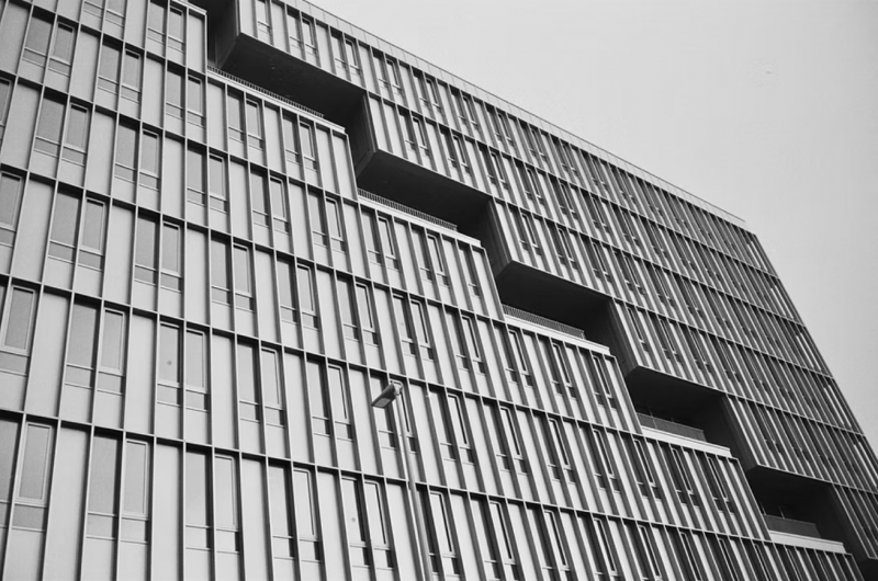 Black and white architectural photograph of a modernist building facade with stepped recesses and vertical window grilles.
